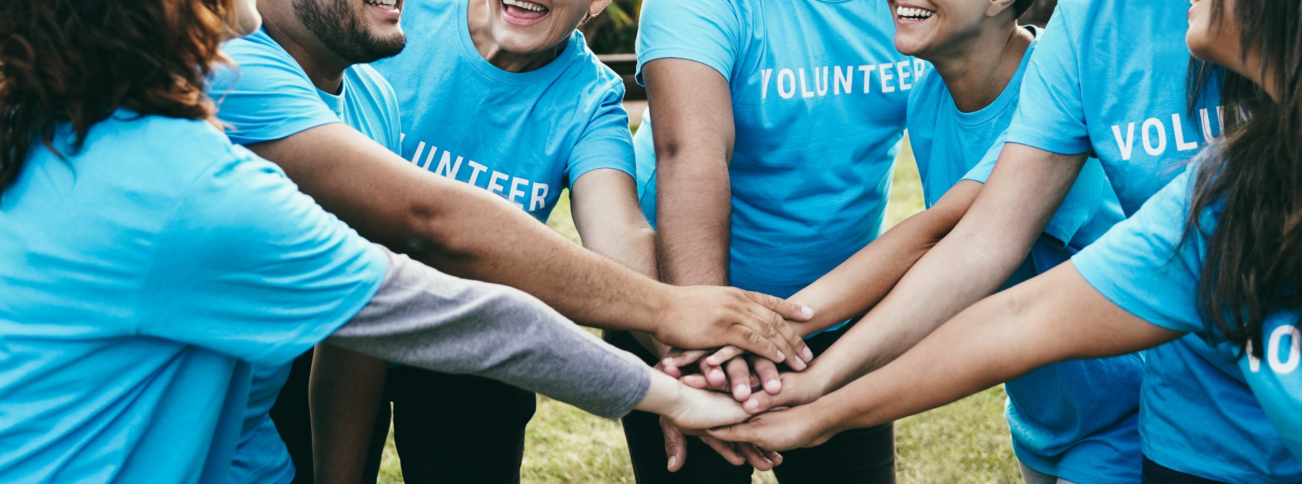 Happy group of volunteer people stacking hands celebrating together outdoor - Teamwork and charity support concept - Focus on back faces